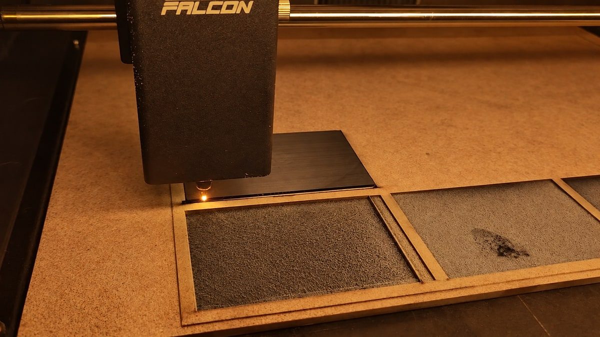 Falcon laser machine working on a metal card, viewed through its amber protective cover.